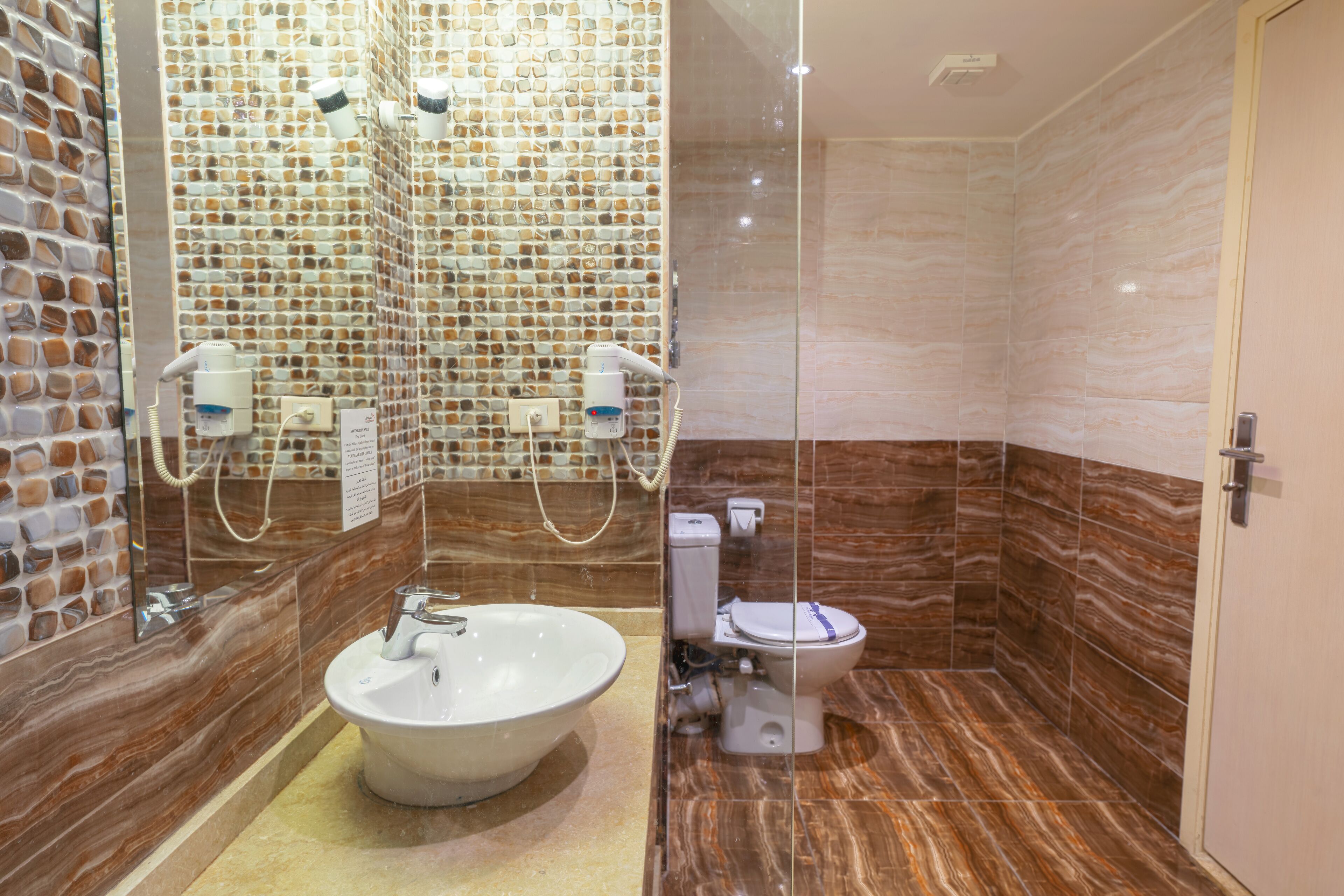 Et badeværelse med vask i marmor, toilet og brusekabine med mosaikfliser.