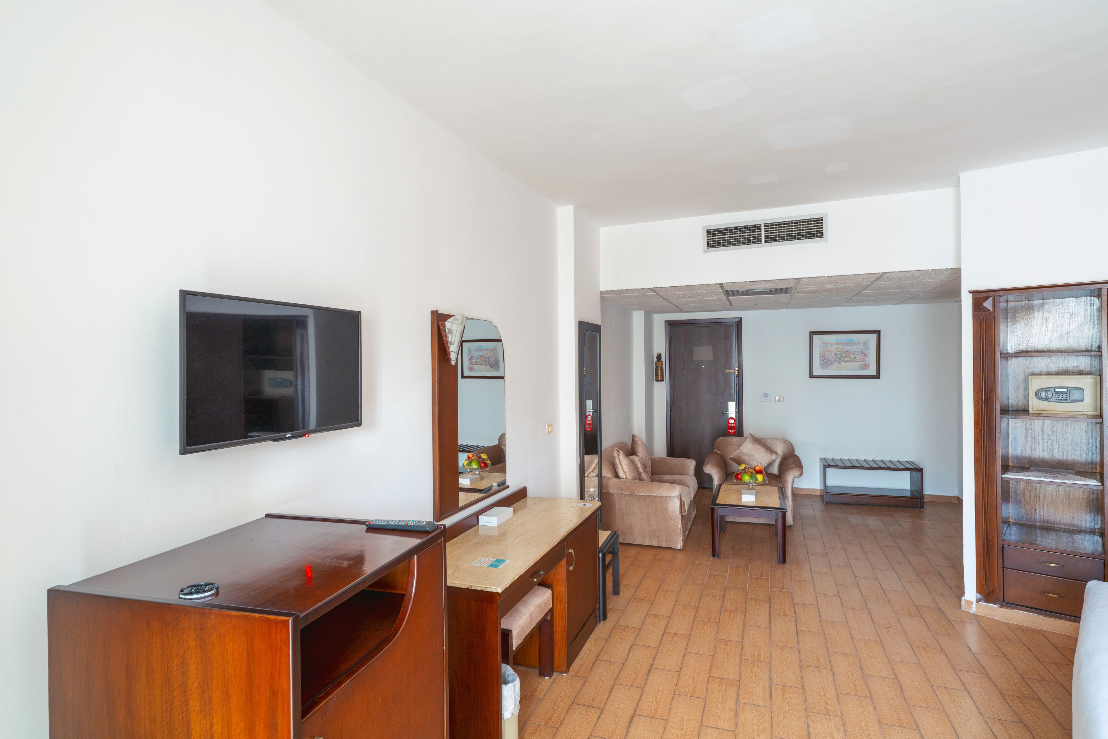 Un espacio habitable compacto con un escritorio de madera, un televisor montado en la pared, un sofá y una pequeña mesa con un jarrón.