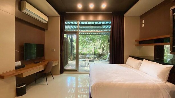 A modern hotel room with a large bed, a desk, a TV, and a sliding glass door leading to an outdoor area.