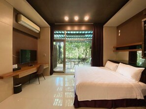 A modern hotel room with a large bed, a desk, a TV, and a sliding glass door leading to an outdoor area.