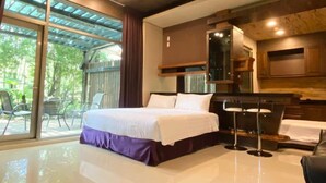 A modern hotel room with a large bed, a built-in TV, and a balcony with outdoor seating.