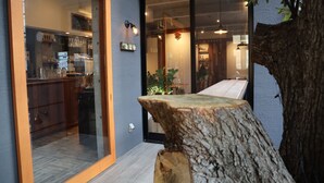 A modern interior with a large glass door leading to a kitchen area, a wooden tree stump table, and a view of the dining area through the glass. - Treeside Hotel & Apartment (Yugawara)