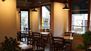 A restaurant interior with wooden tables and chairs, potted plants, and hanging pendant lights. - Treeside Hotel & Apartment (Yugawara)