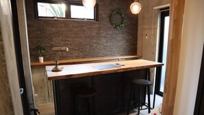 A kitchen with a wooden countertop, two bar stools, a potted plant, and a brick wall. - Treeside Hotel & Apartment (Yugawara)