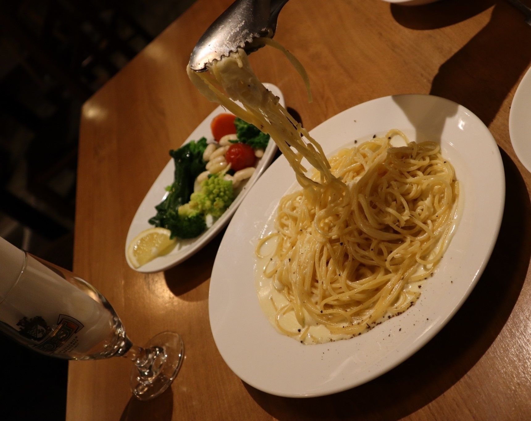 A plate of spaghetti with a side salad and a glass of wine on a wooden table.