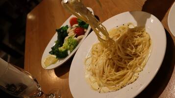 A plate of spaghetti with a side salad and a glass of wine on a wooden table.