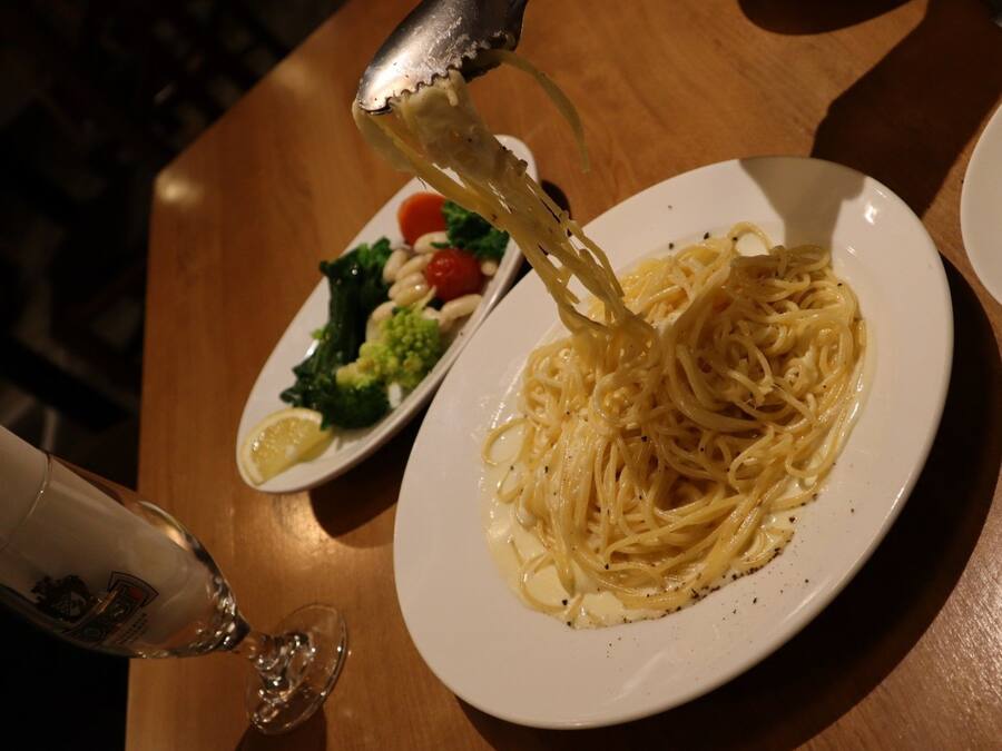 A plate of spaghetti with a side salad and a glass of wine on a wooden table.