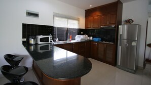 A kitchen with a black granite countertop, stainless steel appliances, and wooden cabinets. - Bali Tropicana Pool Villa (Pattaya)