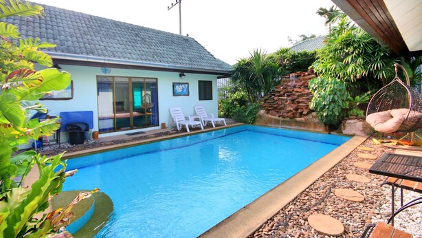 A swimming pool with a tiled roof, two lounge chairs, and a hanging chair. - Bali Tropicana Pool Villa (Pattaya)