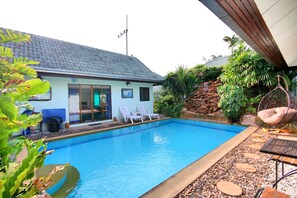 A swimming pool with a tiled roof, two lounge chairs, and a hanging chair. - Bali Tropicana Pool Villa (Pattaya)