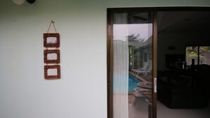 A room with a sliding glass door leading to a pool area, a small table, and a sofa. - Bali Tropicana Pool Villa (Pattaya)