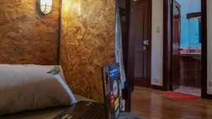 Habitación de hotel con pared de madera, cama con almohadas, una laptop sobre una silla y una puerta que da a un baño.