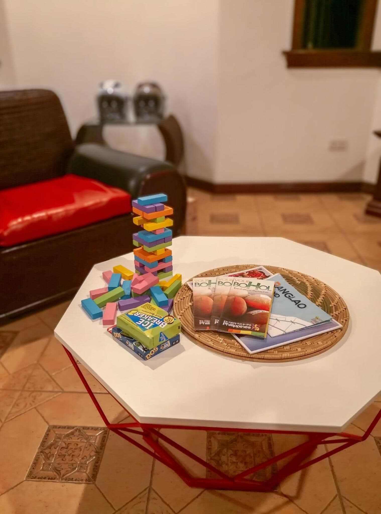 A white table with a stack of colorful building blocks and two books titled "BOHBOH BOHBOH" and "ANGLOA" on a woven placemat.