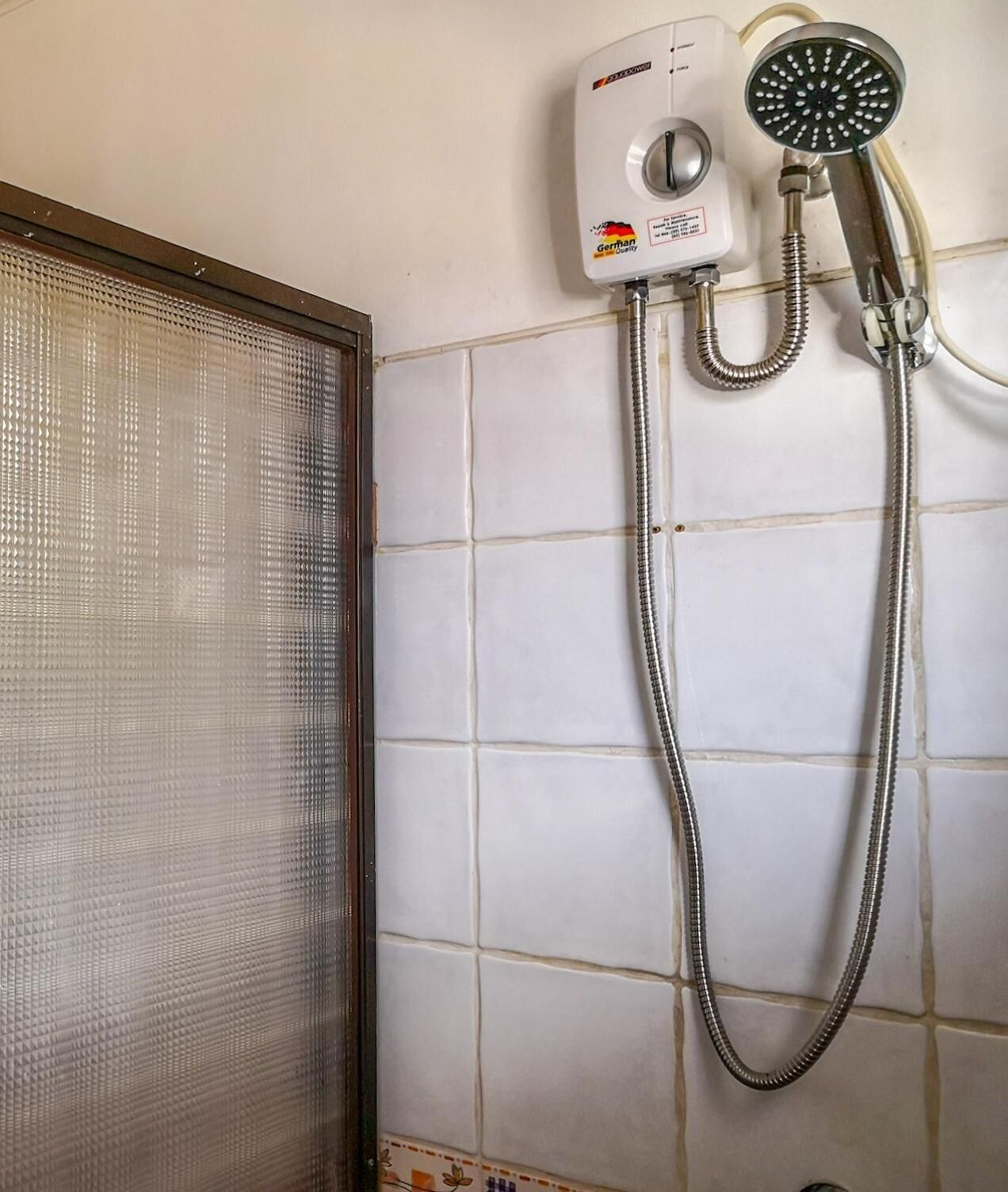 A bathroom with a shower, a toilet, and a window with a metal screen.