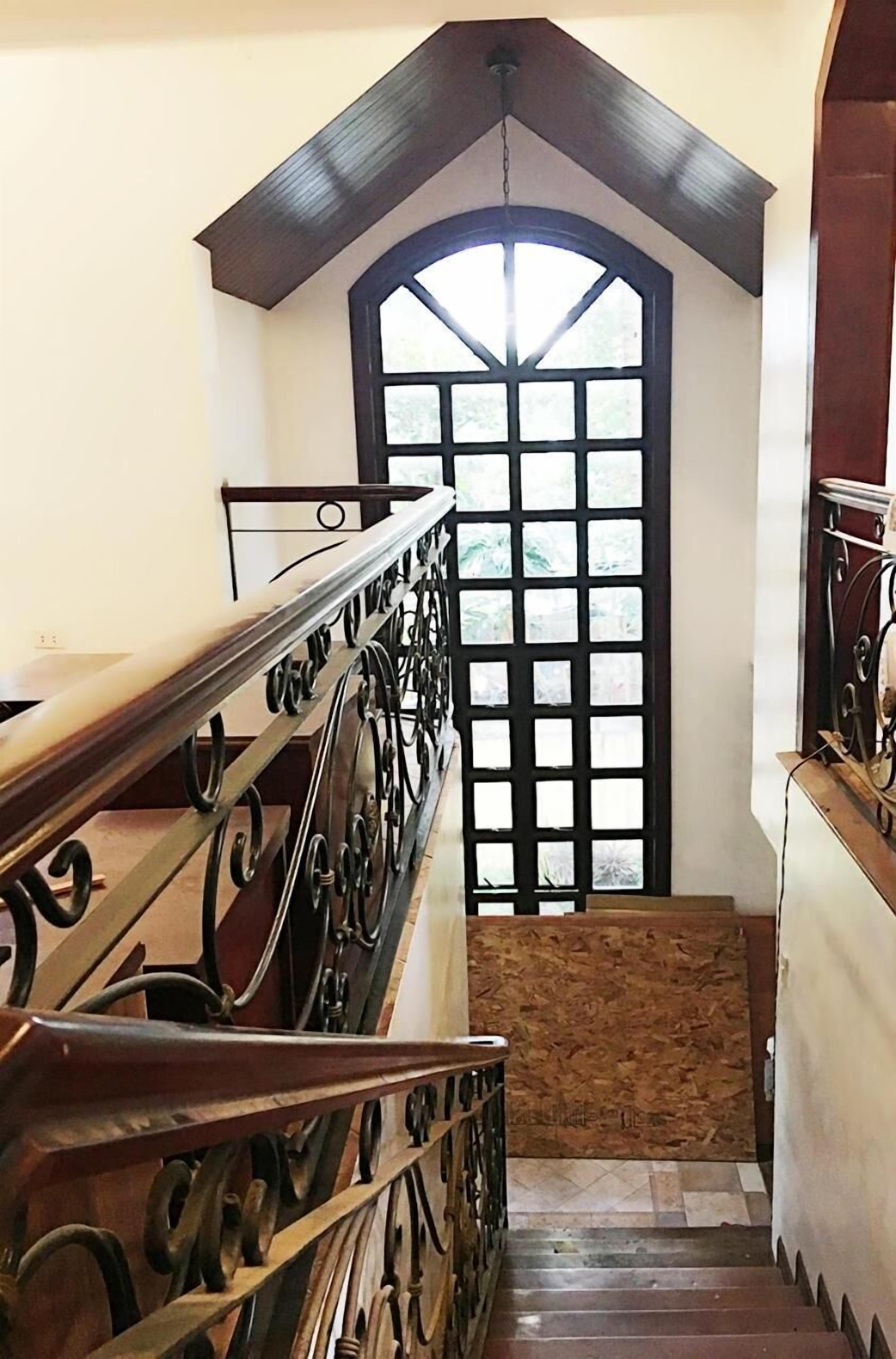 A staircase with a wooden handrail and a black metal railing, leading to a room with a large arched window.