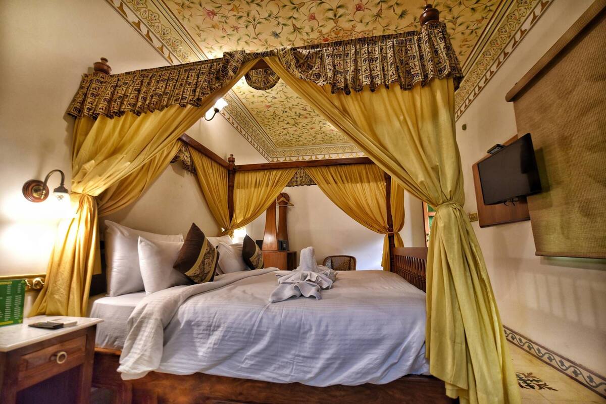 A four-poster bed with yellow curtains, a wooden headboard, and a floral ceiling design.