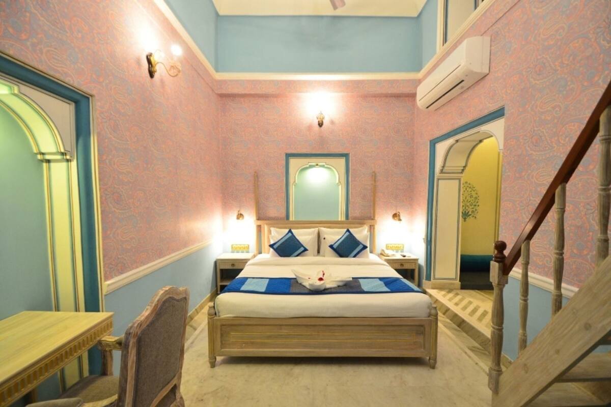 A bedroom with a large bed, bedside tables, a chair, a mirror, and a staircase.