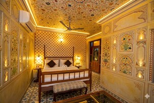 A traditional room with a bed, a bench, patterned walls, and a ceiling fan.