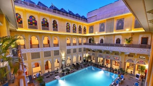 A large indoor swimming pool surrounded by multiple balconies with ornate railings and seating areas. - Nirbana Palace - A Heritage Hotel (Jaipur)