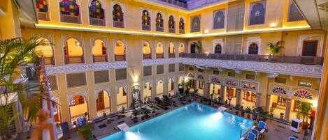 Una amplia piscina interior rodeada de varios balcones con barandillas ornamentales y zonas de estar.