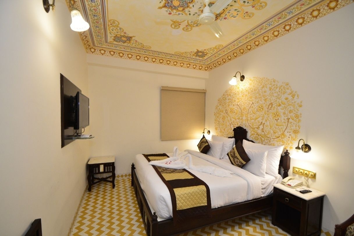 Quarto de hotel com cama, mesa de cabeceira e teto com detalhes elaborados.