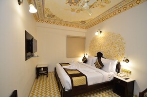 Quarto de hotel com cama, mesa de cabeceira e teto com detalhes elaborados.
