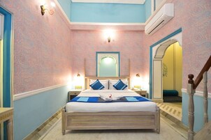 Quarto de hotel com uma cama grande, um espelho em cima e uma escada à direita.