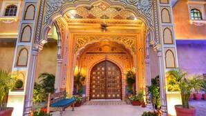 An ornate entrance with a large wooden door, intricate floral and geometric patterns, and potted plants. - Nirbana Palace - A Heritage Hotel (Jaipur)