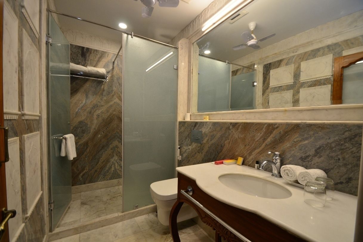 Um banheiro com chuveiro em cabine de vidro, parede com azulejos de mármore, pia com espelho e ventilador de teto.