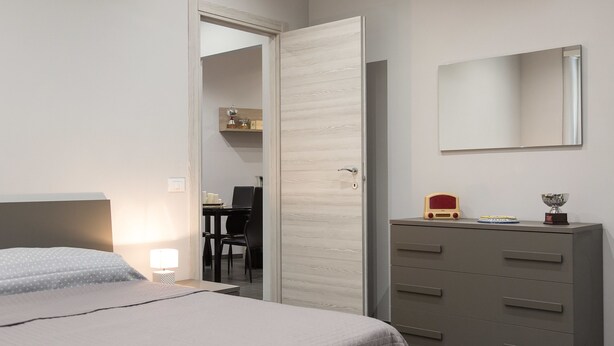 A bedroom with a bed, a dresser, a mirror, and a door leading to another room. - Rental In Rome Apartment Archimede (Rome)