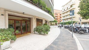 A building with a large entrance, potted plants, and a row of parked motorcycles. - Rental In Rome Apartment Archimede (Rome)