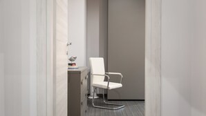 A narrow hallway with a white chair and a small table with a trophy. - Rental In Rome Apartment Archimede (Rome)