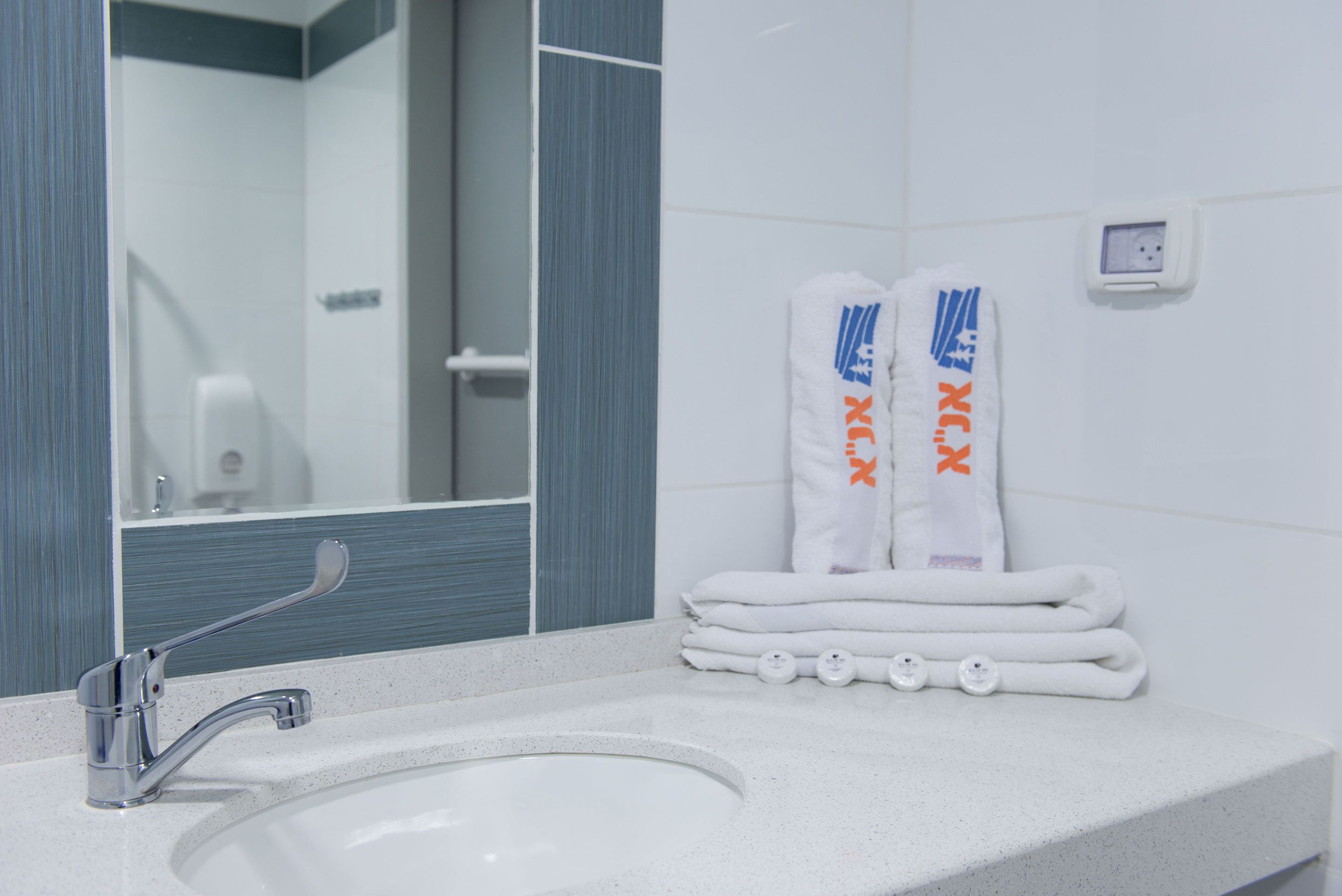 A bathroom with a sink, mirror, towel rack, and a wall socket.