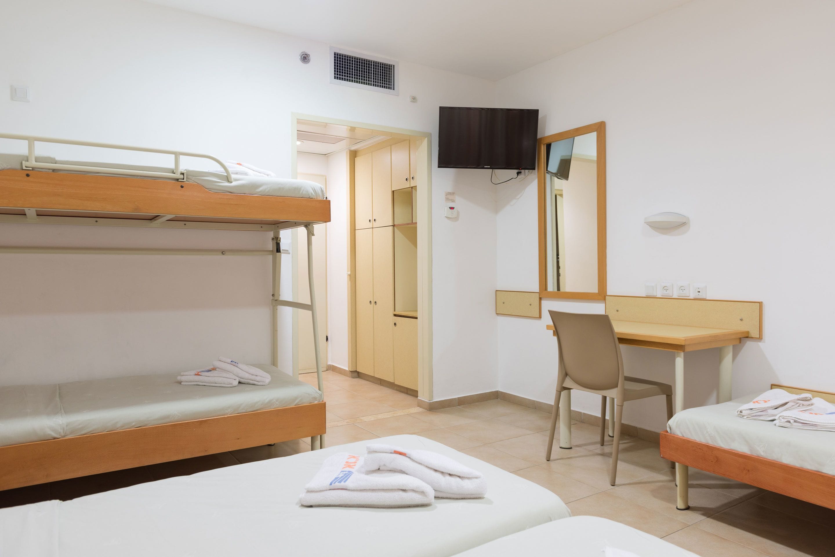 Un dormitorio con literas, un escritorio, una silla y un televisor montado en la pared.