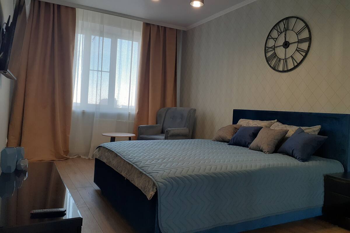 Ein Schlafzimmer mit einem Bett, einem Sessel, einem kleinen Tisch und einer Wanduhr.