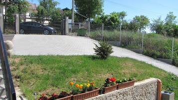 Un camino pavimentado con jardineras de flores, un pequeño árbol y un automóvil estacionado cerca de una entrada con portón.