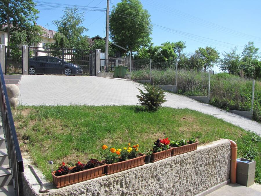 Un camino pavimentado con jardineras de flores, un pequeño árbol y un automóvil estacionado cerca de una entrada con portón.