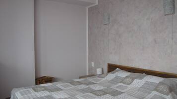 Une chambre à coucher avec un lit en bois, un petit tabouret en bois et un mur sobre agrémenté de deux éléments décoratifs.