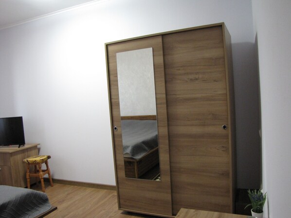 Una habitación con un armario de madera, un taburete pequeño, una cama y un televisor sobre un mueble de madera.