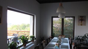 A dining area with a long table, chairs, potted plants, and a view of greenery outside. - Agropensiunea Maris (Feleacu)