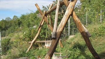 A wooden structure with a swing set, surrounded by greenery and a fence.