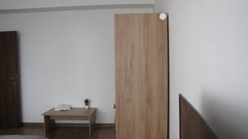 A bedroom with a wooden headboard, a bedside table with a plant, a bed with a gray blanket, and a wooden floor.