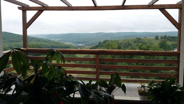 A wooden balcony with a view of rolling hills and a valley. - Agropensiunea Maris (Feleacu)