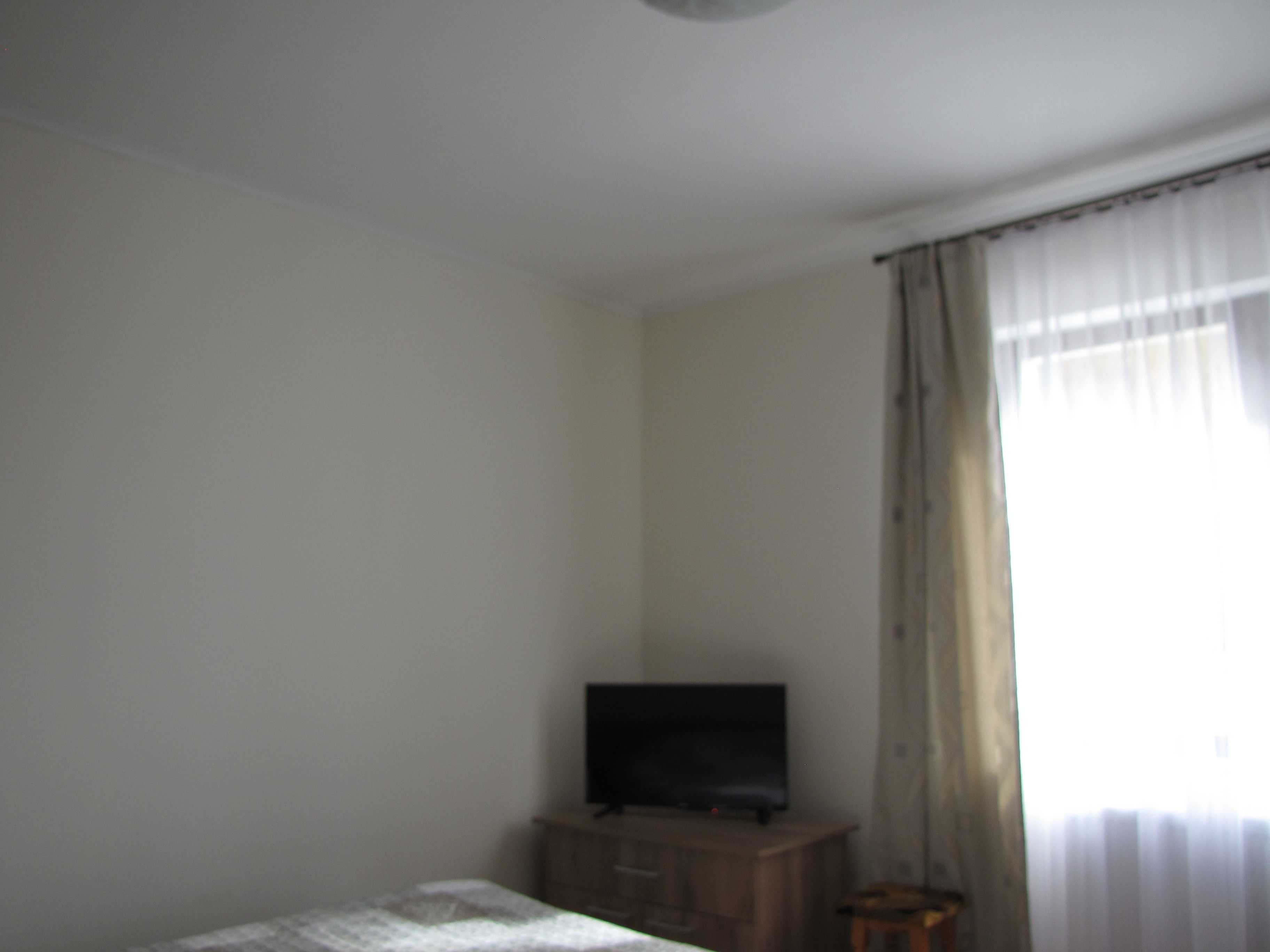 Una habitación con una cama, un televisor sobre un mueble de madera y una ventana con cortinas.