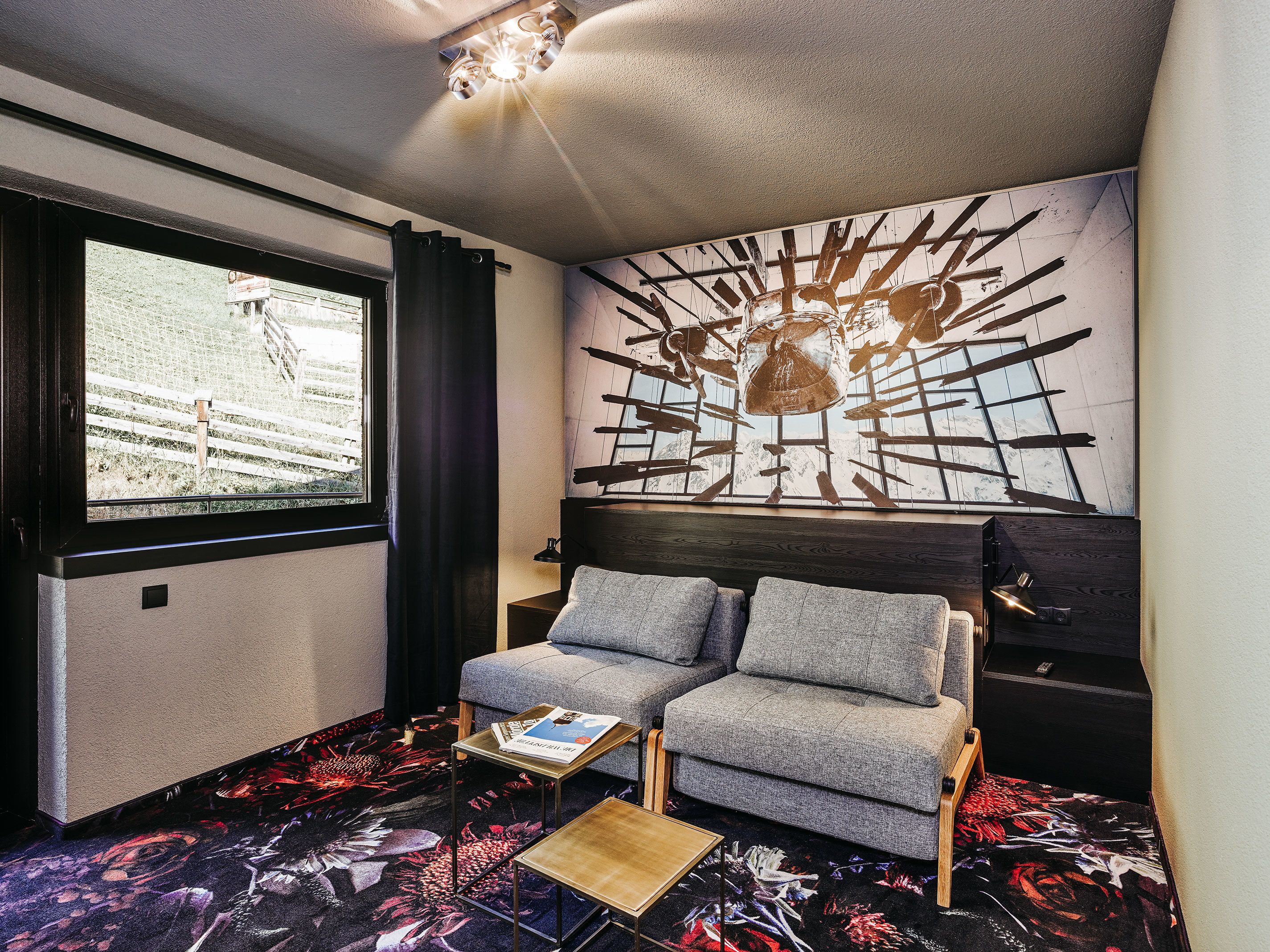 A modern room with a large window, a projector screen, a sofa, a coffee table, and a unique wall art piece.