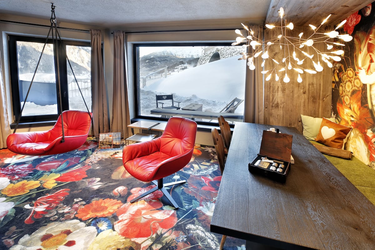 A room with a large window, red chairs, a wooden table, and a floral carpet.