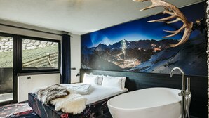 Une salle de bain moderne avec une grande baignoire, une tête de cerf fixée au mur et une fresque représentant un paysage de montagne.