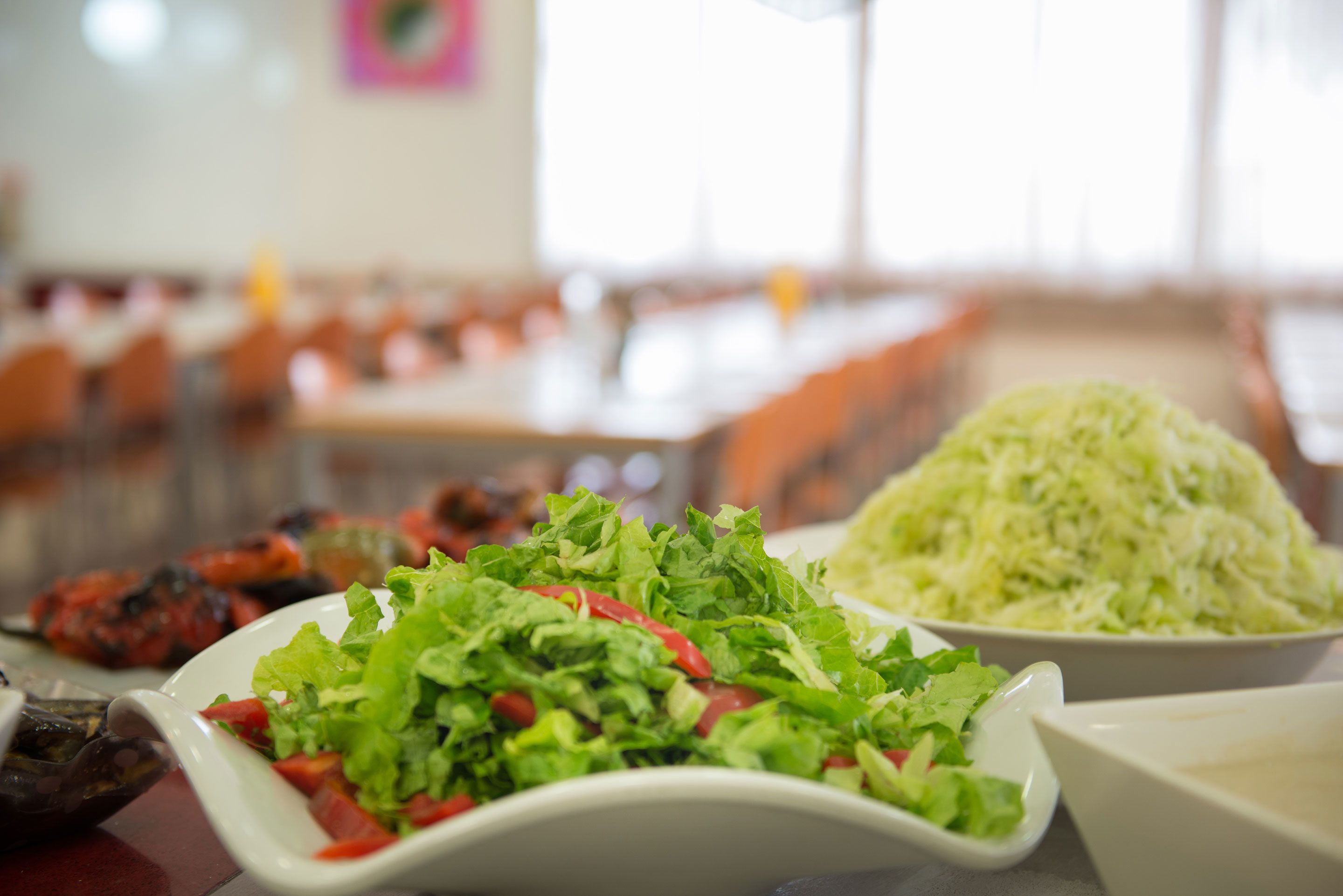 Un comedor con mesas dispuestas para comidas, incluyendo un plato de ensalada y un tazón de col rallada.