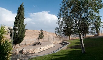 A park with a stone bench, a picnic table, and a fenced area with trees.