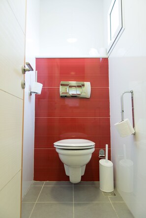 Une salle de bain avec des toilettes blanches, des carreaux rouges, un sèche-mains et un distributeur de serviettes en papier.